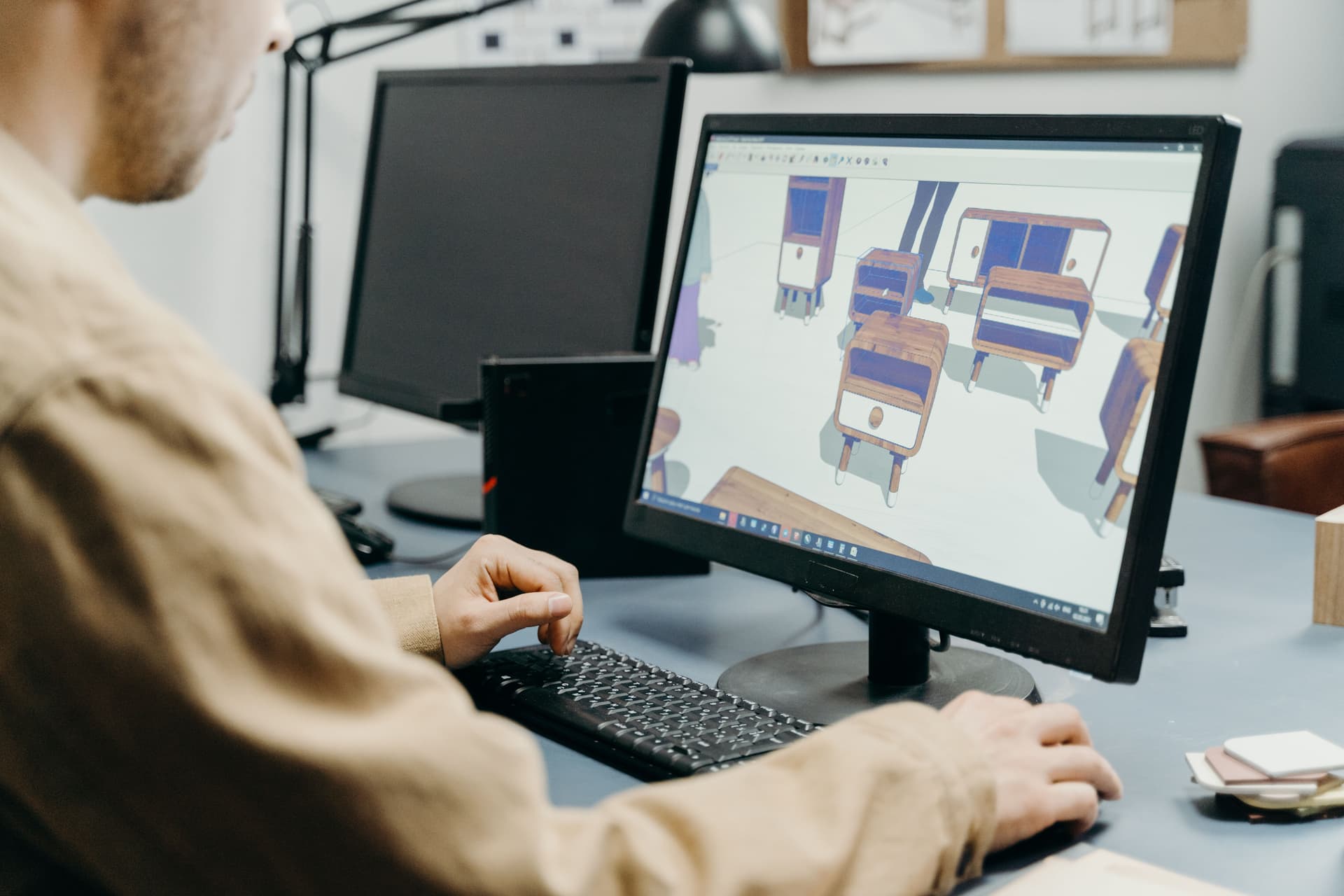 Interior designer working at a computer screen with specification documents, representing FF&E specification software in use
